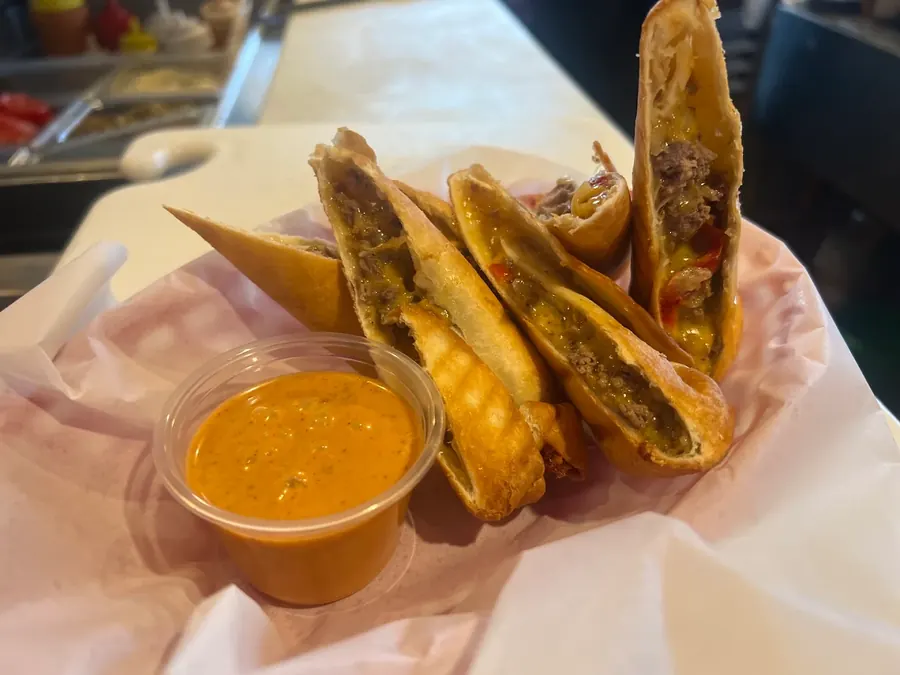 Cheesesteak egg rolls cut open with a cup of spicy dipping sauce